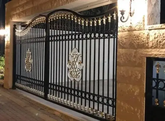 שער חנייה רחב עם עיטורי פליז מוזהבים על רקע אבן ירושלמית